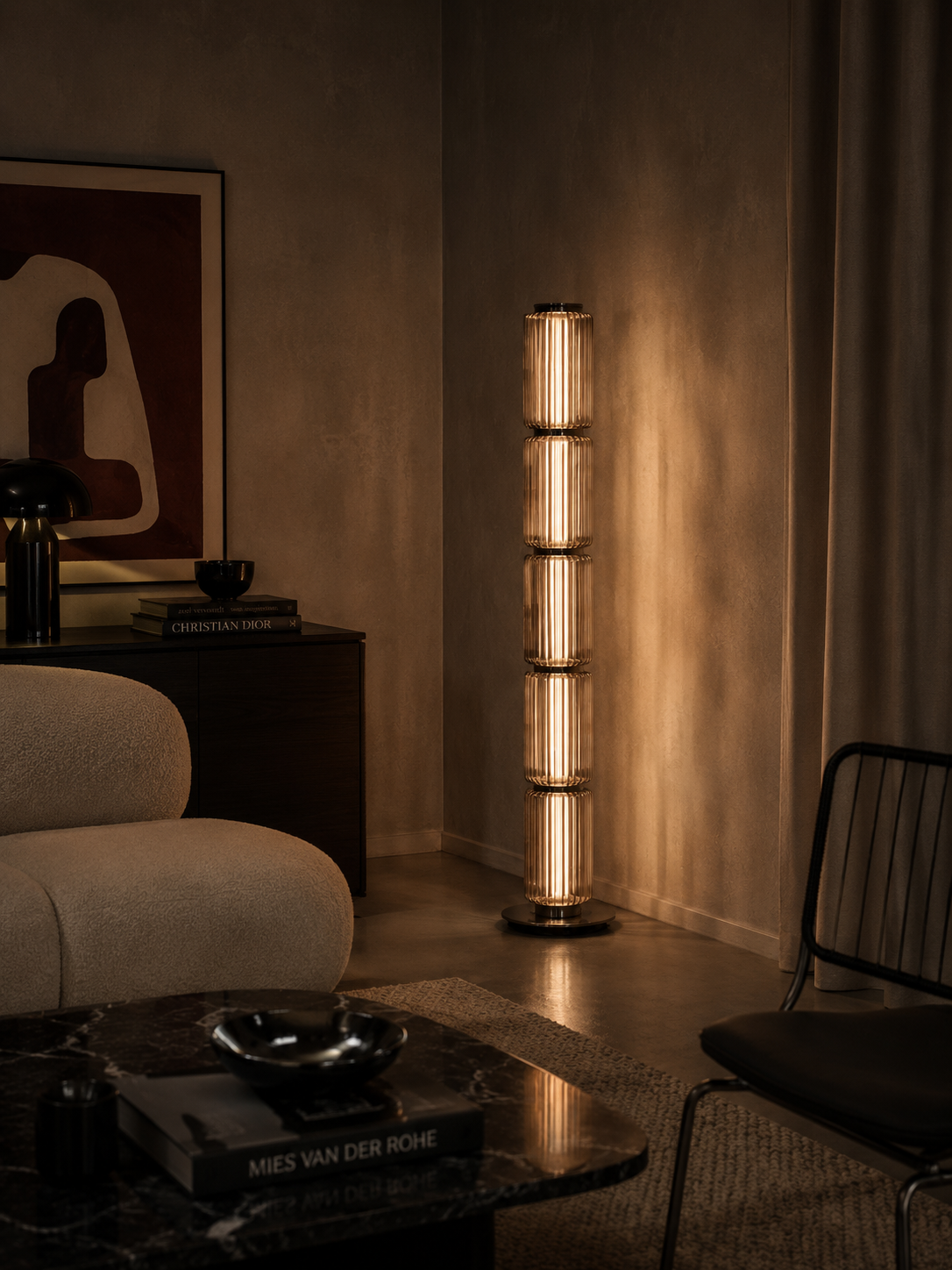 A modern cylindrical floor lamp with stacked glass panels and warm glowing bulbs, standing in a dimly lit living room corner next to a sofa and coffee table.